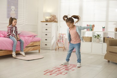 Photo of Cute little girls playing hopscotch at home