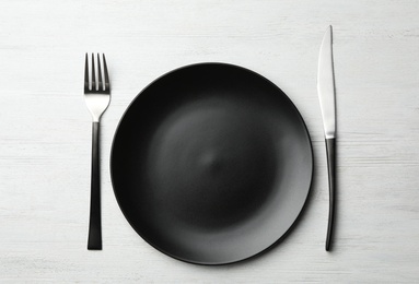 Stylish ceramic plate and cutlery on white wooden background, flat lay