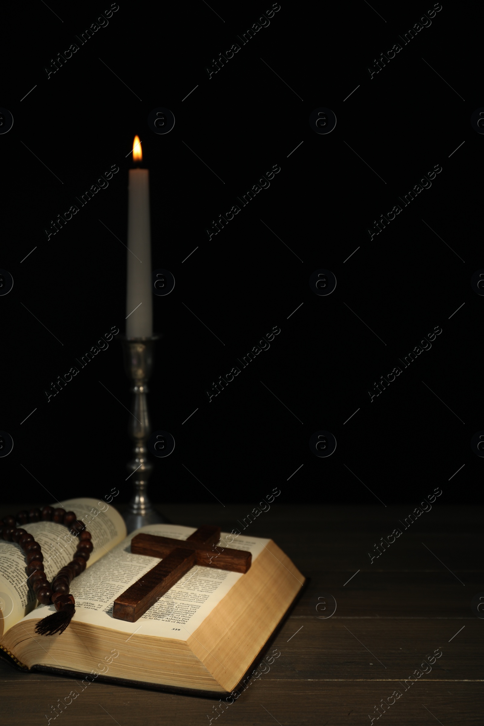 Photo of Church candle, Bible, rosary beads and cross on wooden table against black background, space for text
