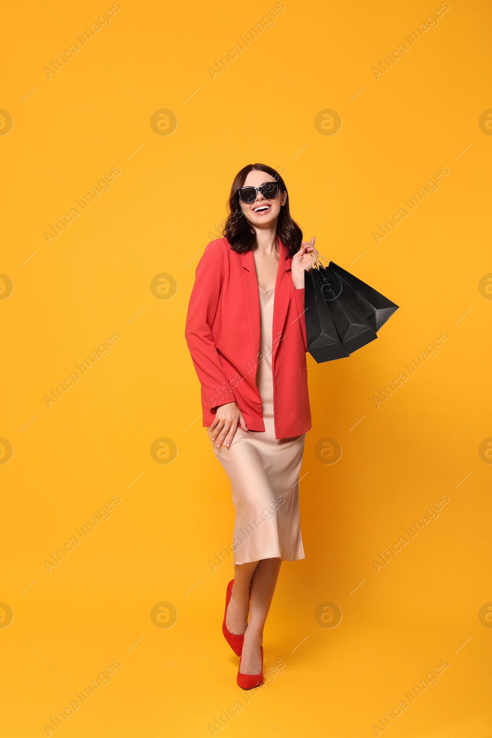 Photo of Beautiful young woman with paper shopping bags on yellow background