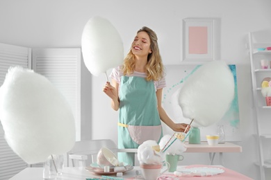 Happy young woman with cotton candy and sweets on table in room