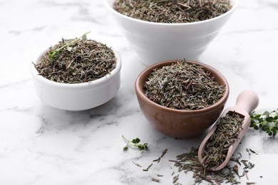 Bowls and scoop with dried thyme on white marble table, closeup