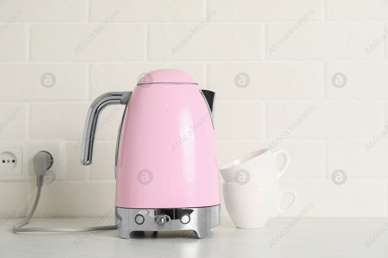 Photo of Modern electric kettle and cups on counter in kitchen