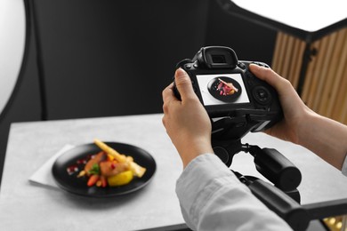 Photo of Woman taking picture of dish with chicken, parsnip and strawberries on grey table in professional photo studio, closeup. Food stylist