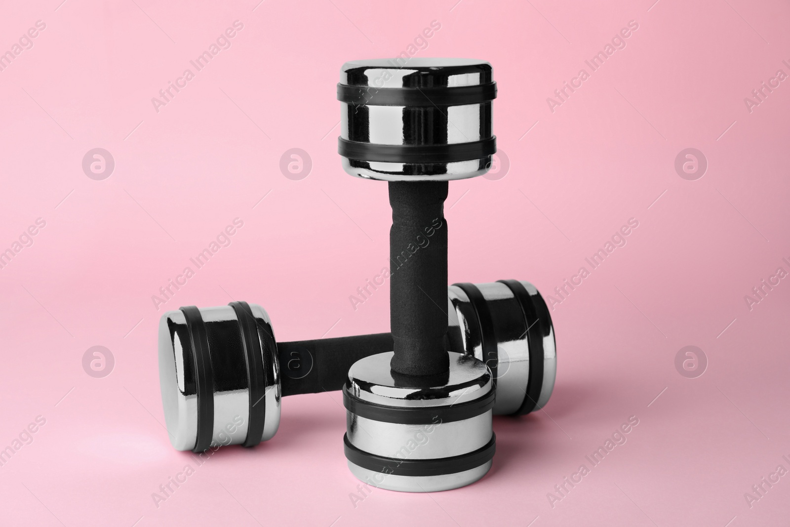 Photo of Dumbbells on light pink background. Weight training equipment