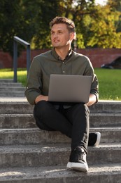 Photo of Handsome man with laptop sitting on concrete stairs outdoors