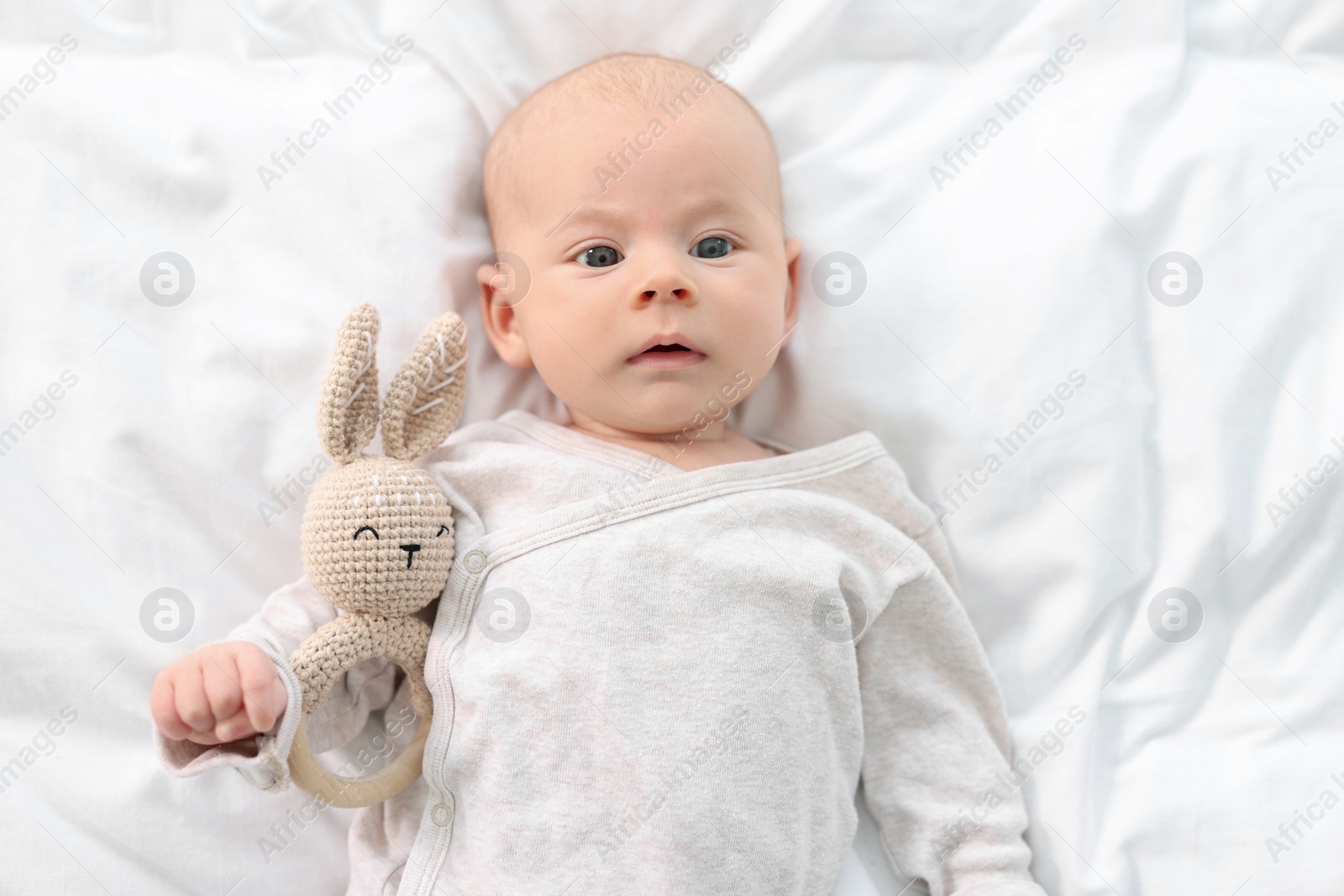 Photo of Cute little baby with toy lying on white sheets, top view