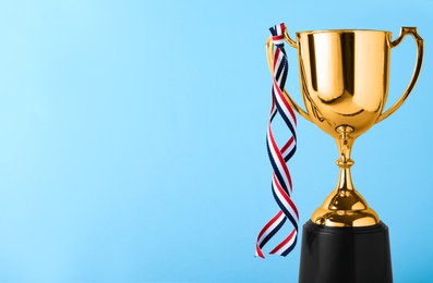 Photo of Golden trophy cup with ribbon on blue background. Space for text