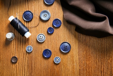 Thread, fabric and buttons for tailoring on wooden background