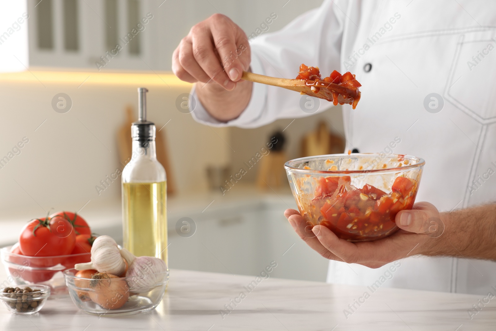 Photo of Professional chef making delicious tomato sauce at white marble table indoors, closeup