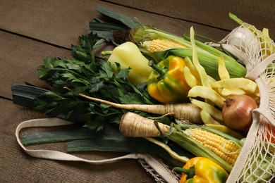 Photo of Different fresh ripe vegetables in net bag on wooden table, closeup