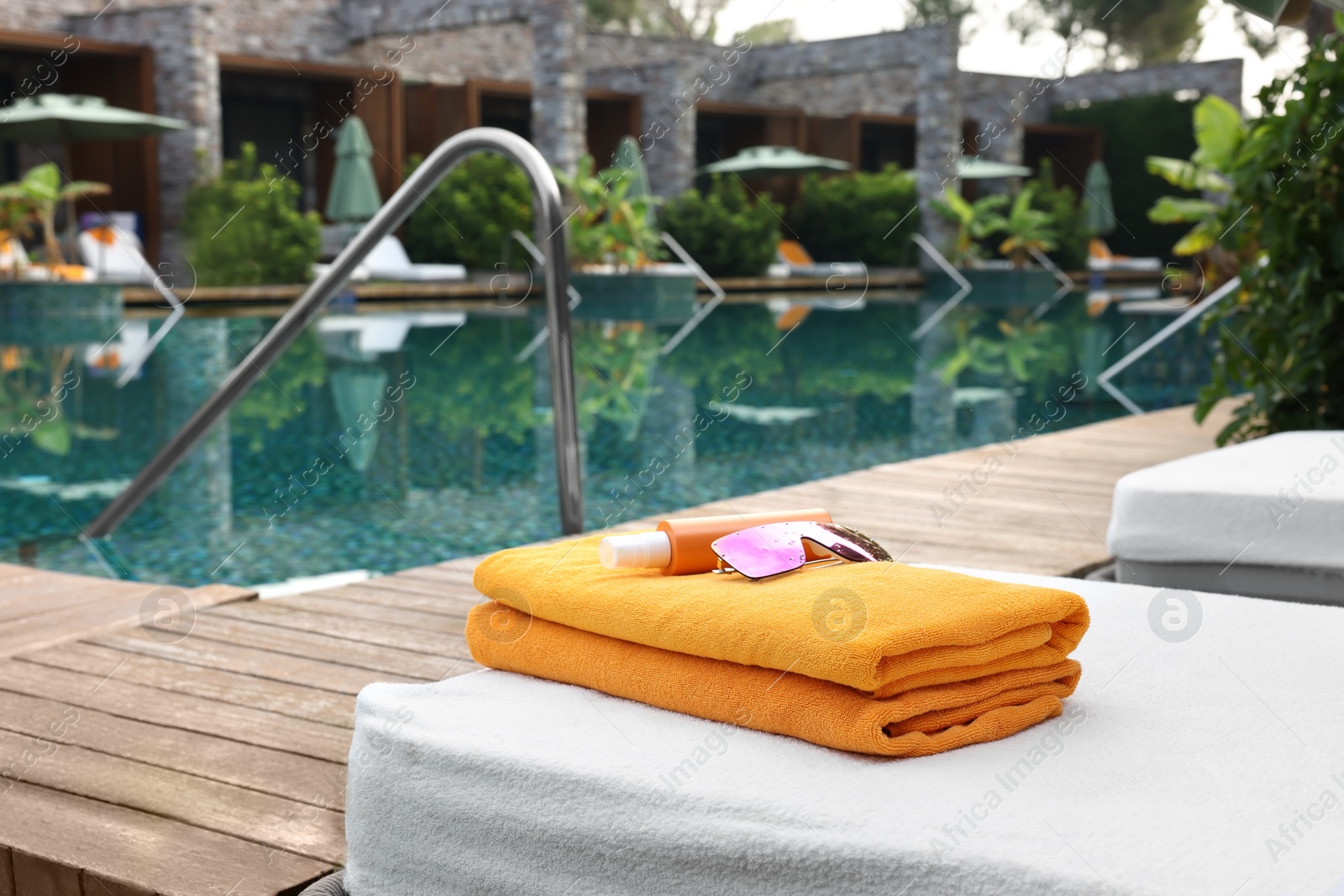 Photo of Beach towels, sunglasses and sunscreen on sun lounger near outdoor swimming pool, space for text. Luxury resort