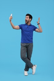 Photo of Surprised man taking selfie with smartphone on light blue background