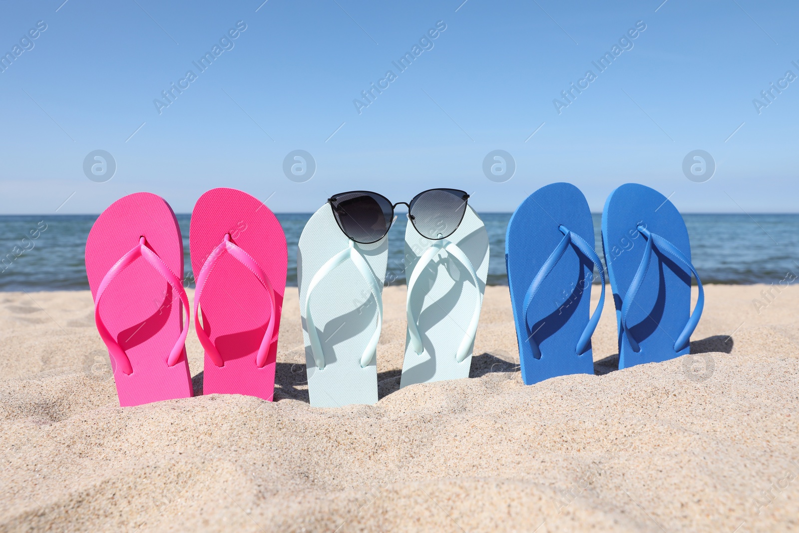 Photo of Stylish colorful flip flops and sunglasses on beach sand