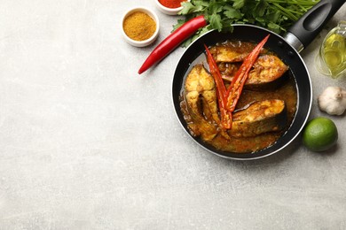 Photo of Tasty fish curry in frying pan and ingredients on light grey table, flat lay. Space for text. Indian cuisine
