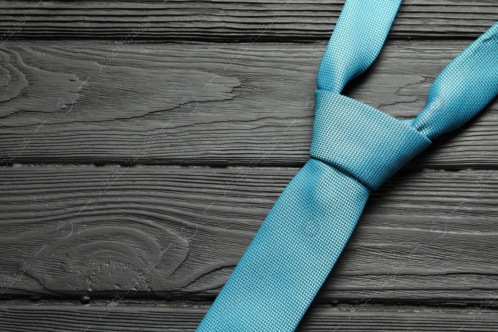 Photo of One light blue necktie on black wooden table, top view. Space for text