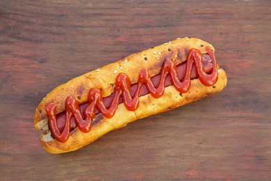 Photo of Fresh tasty hot dog with ketchup on wooden table, top view