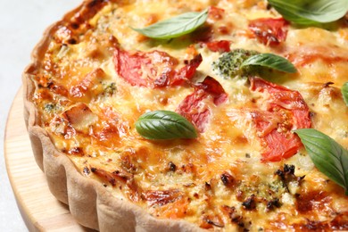 Tasty quiche with cheese, tomatoes and basil leaves on table, closeup