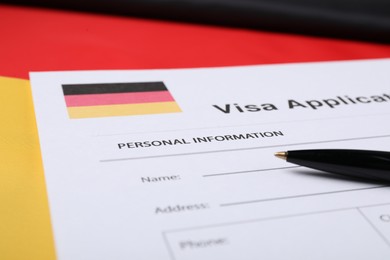 Photo of Immigration to Germany. Visa application form and pen on flag, closeup