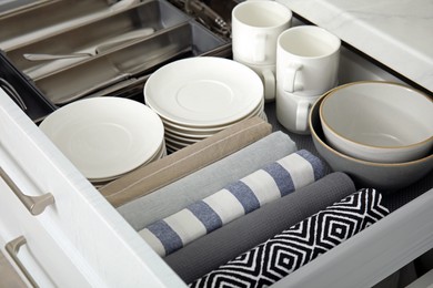 Photo of Open drawer of kitchen cabinet with different dishware and towels, closeup