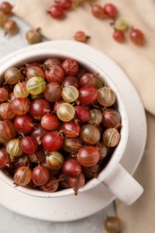 Photo of Cup with ripe gooseberries on light grey table, flat lay