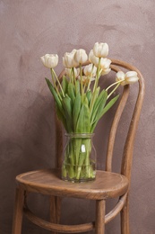 Photo of Vase with beautiful tulips on chair, indoors