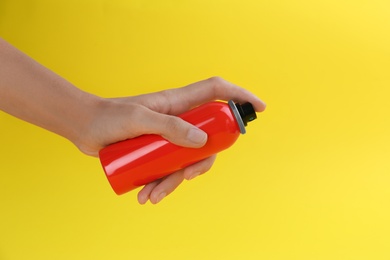 Woman with bottle of insect repellent spray on yellow background, closeup