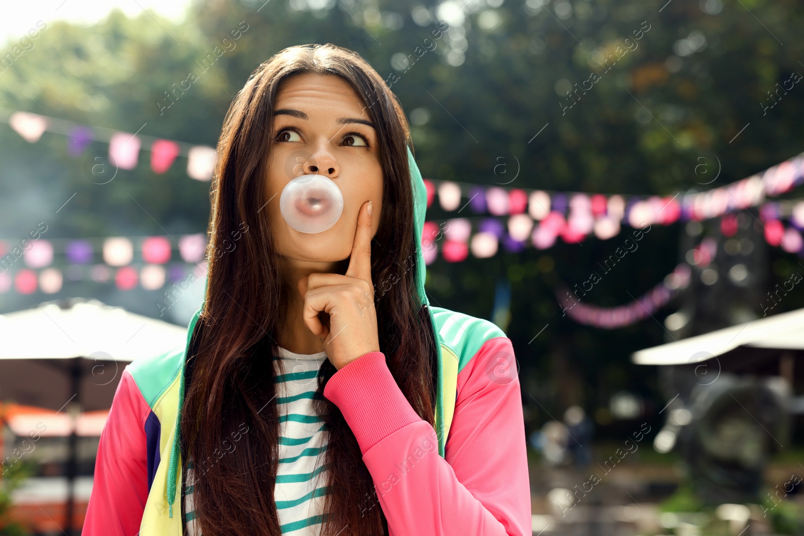 Photo of Beautiful young woman blowing chewing gum on city street outdoors