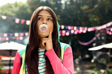 Photo of Beautiful young woman blowing chewing gum on city street outdoors