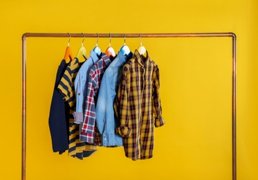 Photo of Rack with stylish children clothes on yellow background