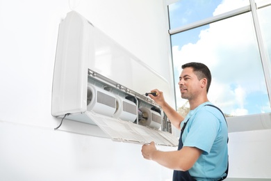 Photo of Male technician fixing modern air conditioner indoors