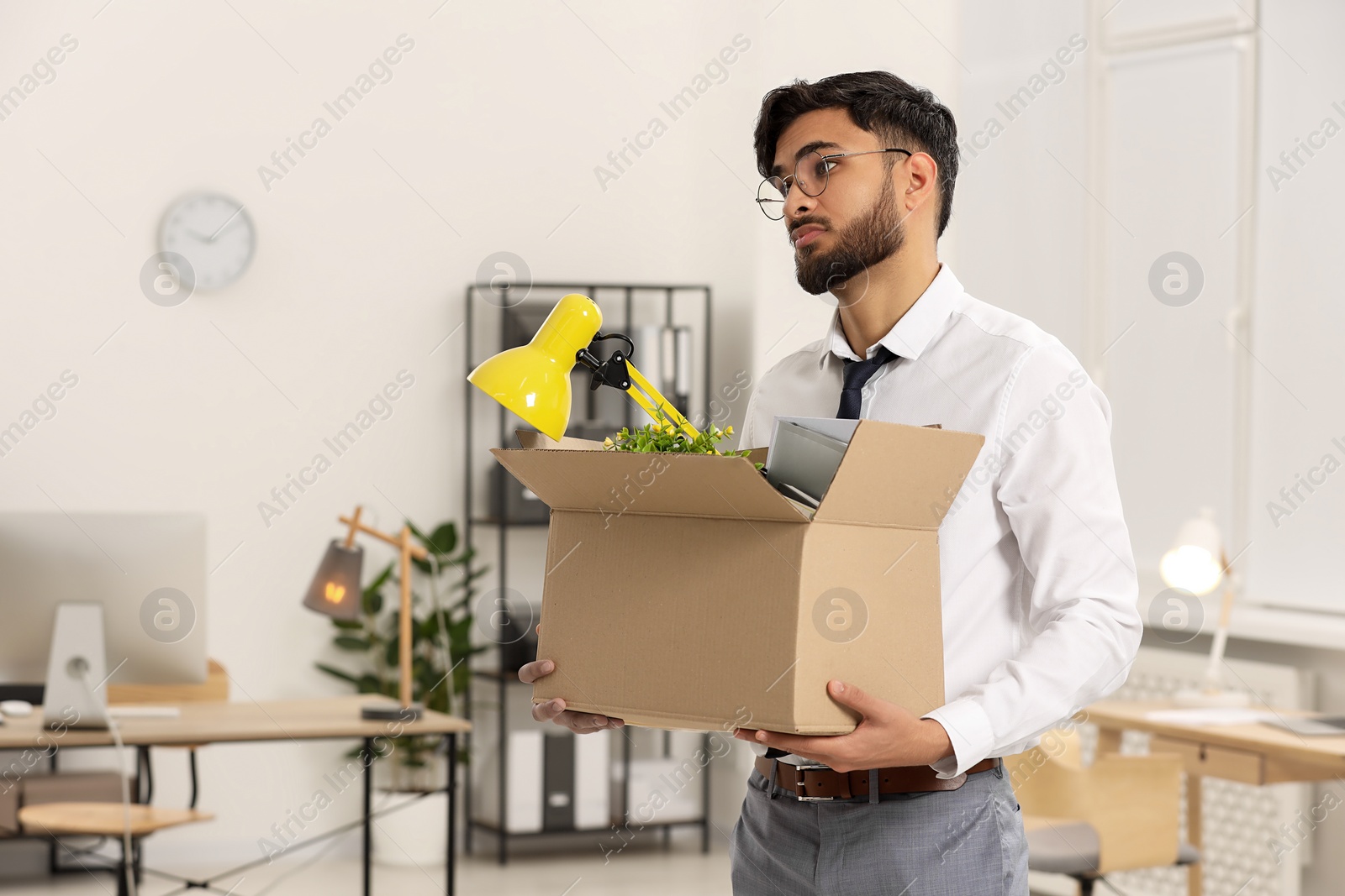 Photo of Unemployment problem. Frustrated man with box of personal belongings in office