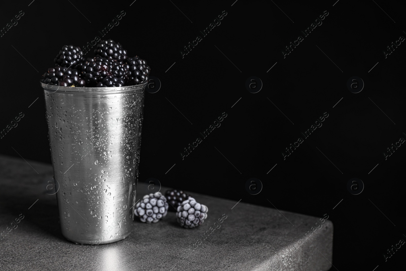 Photo of Fresh and frozen blackberries on grey table against dark background. Space for text