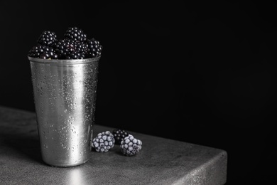 Fresh and frozen blackberries on grey table against dark background. Space for text