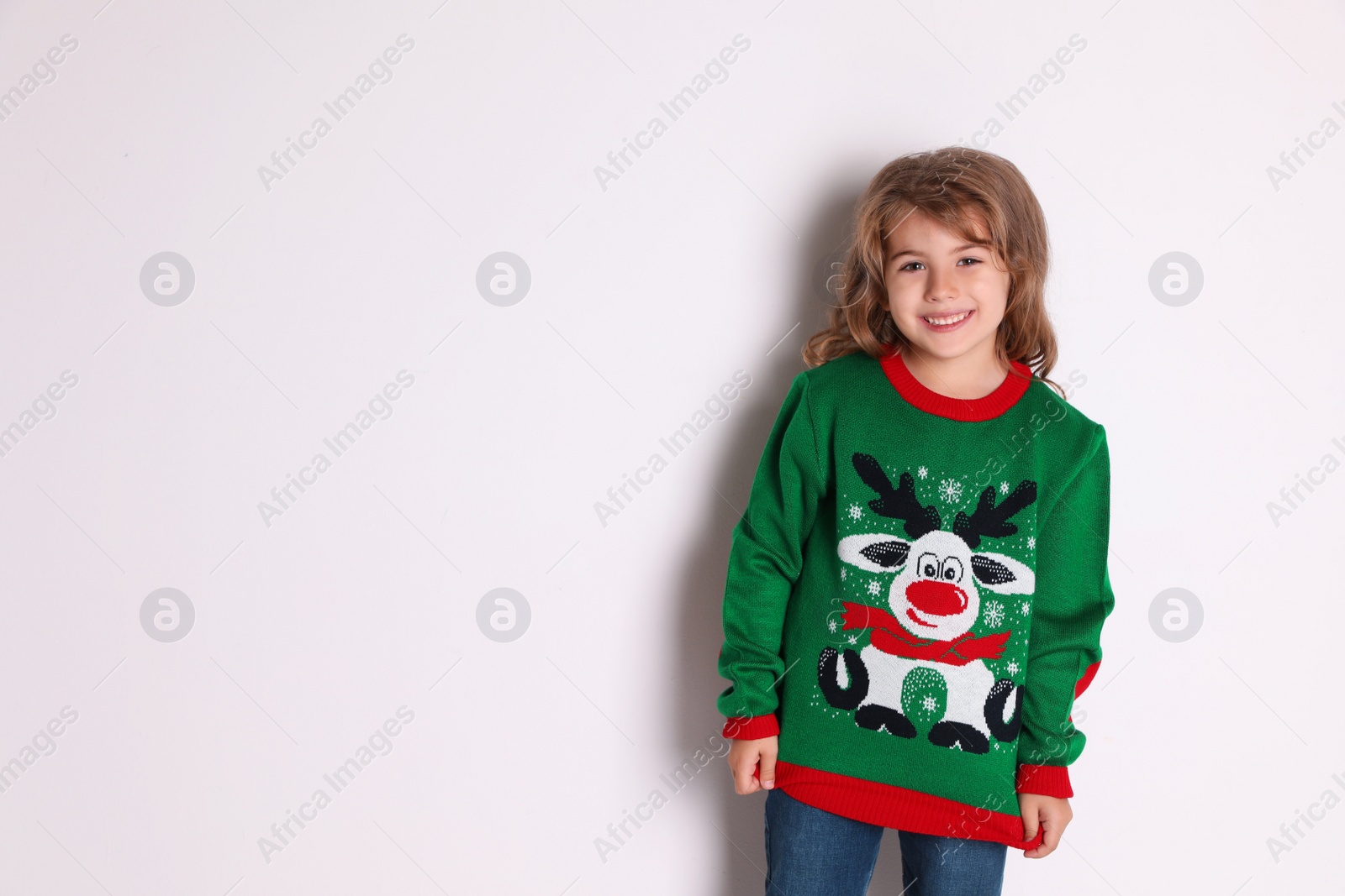 Photo of Cute little girl in green Christmas sweater smiling against white background
