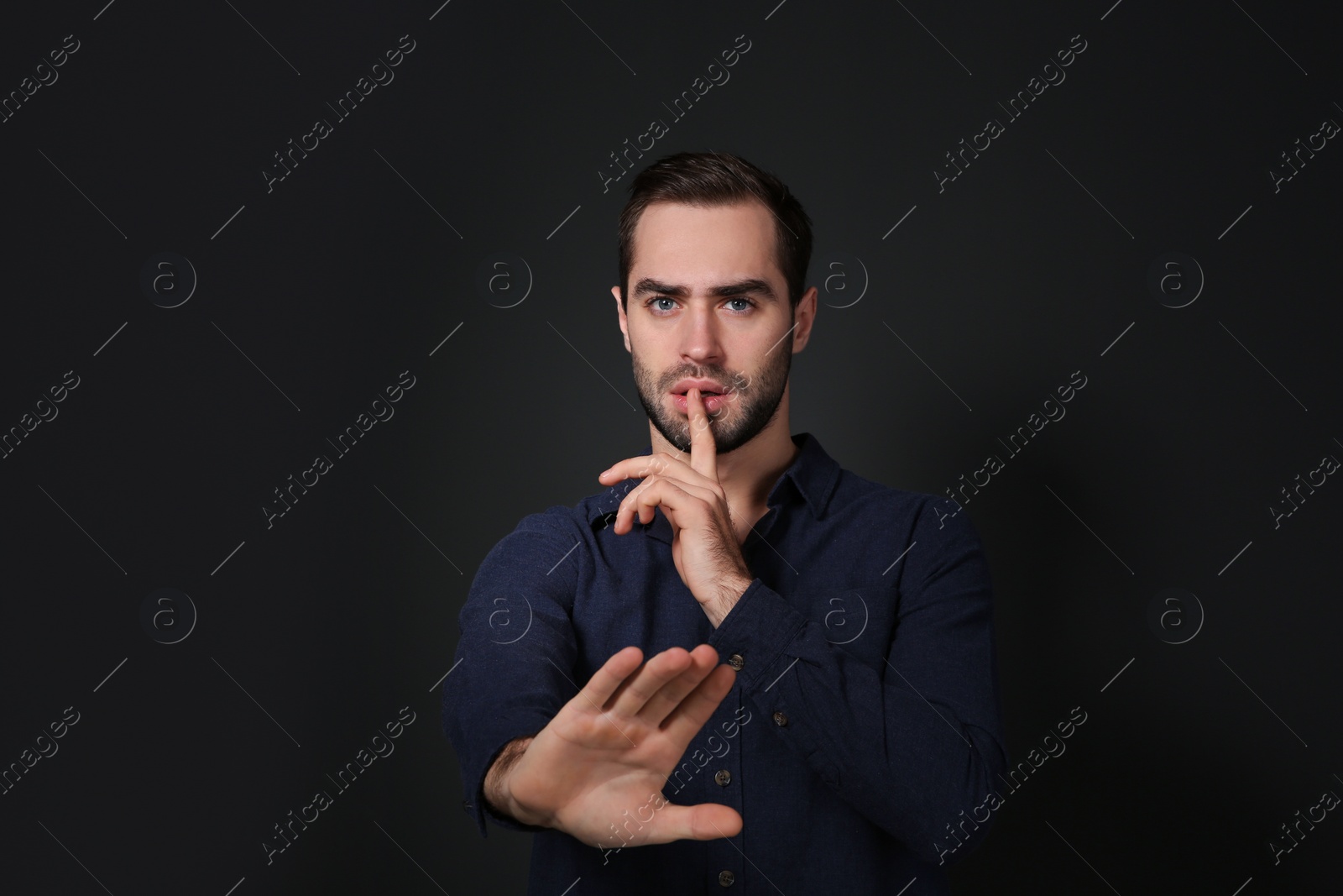 Photo of Man showing HUSH gesture in sign language on black background