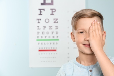 Photo of Cute little boy covering eye in ophthalmologist office