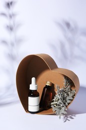 Photo of Heart shaped box with cosmetic products and silver leaves on white background