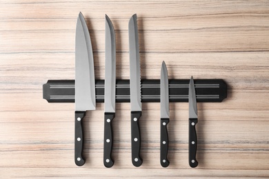 Photo of Magnetic holder with set of knives on wooden background