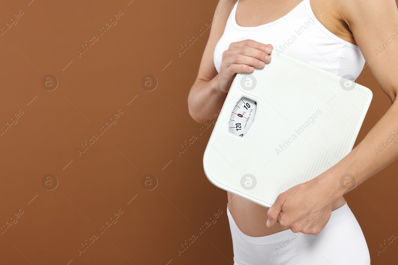 Photo of Slim woman holding scales on brown background, closeup and space for text. Weight loss