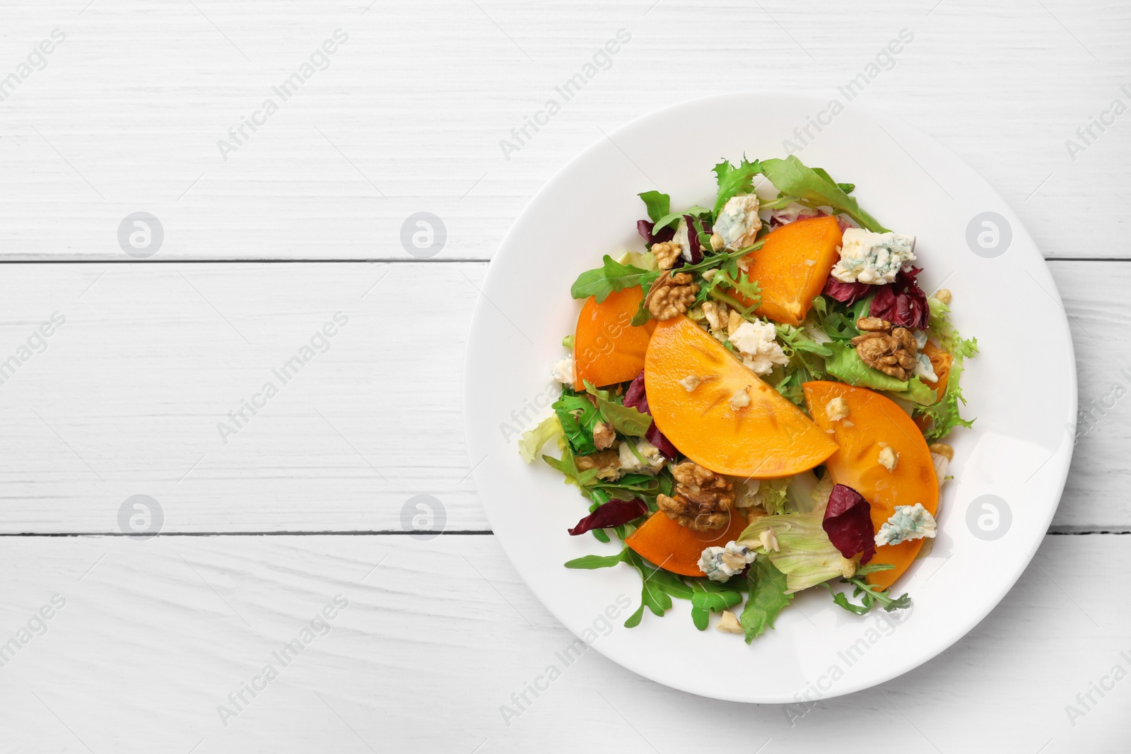 Photo of Delicious persimmon salad with arugula and cheese on white wooden table, top view. Space for text