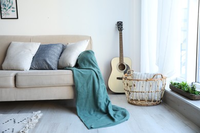 Photo of Guitar near comfortable sofa with cushions and plaid in stylish living room interior