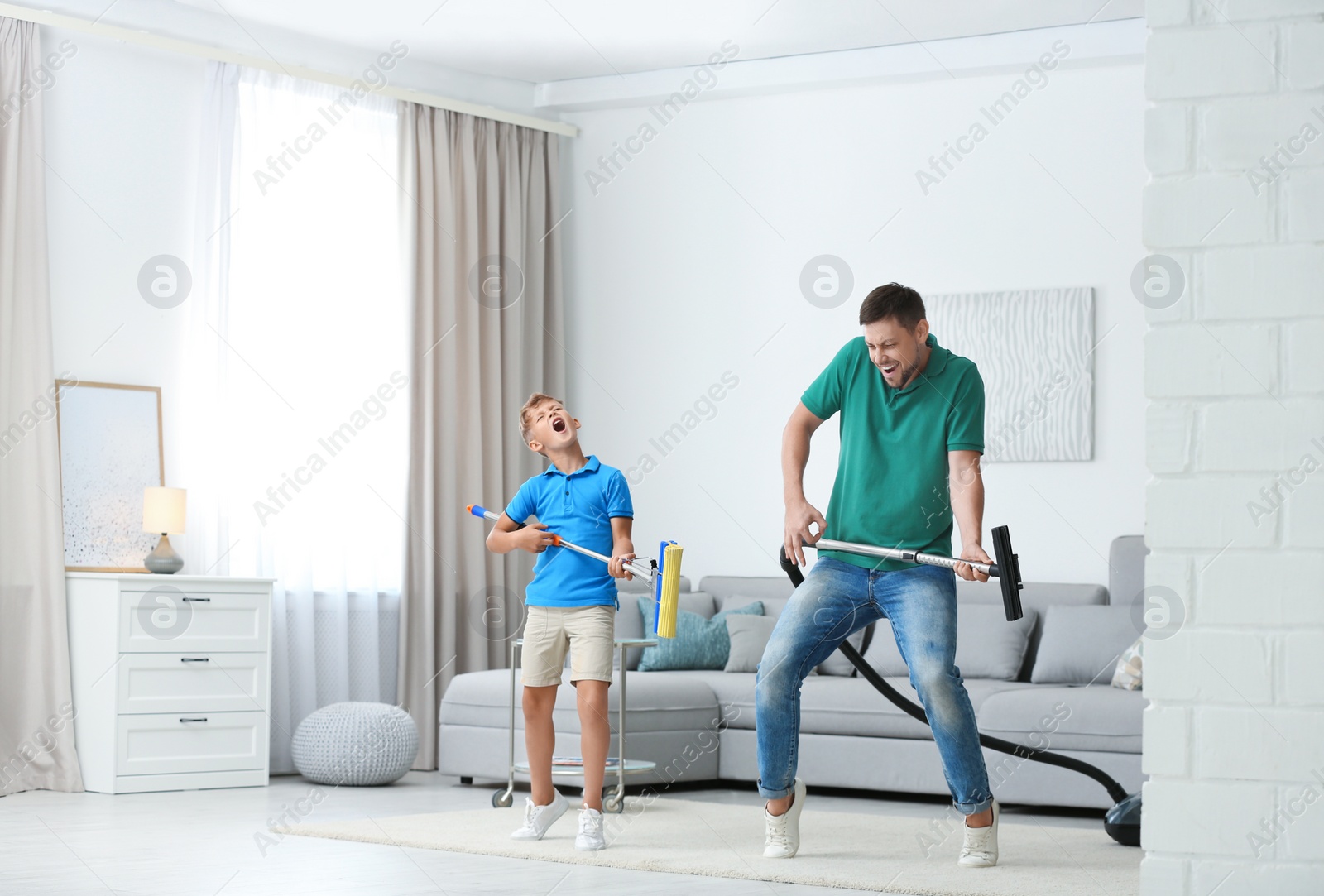 Photo of Dad and son having fun while cleaning living room together