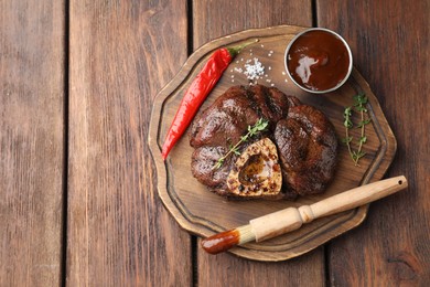 Delicious roasted beef meat served with sauce and spices on wooden table, top view. Space for text