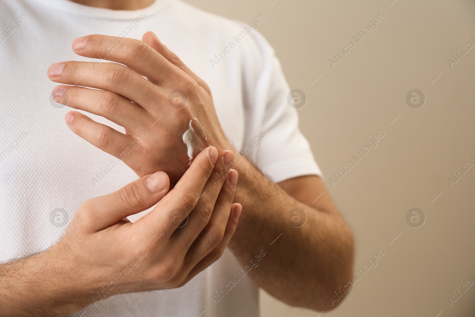 Photo of Man applying cream onto hand on beige background, closeup