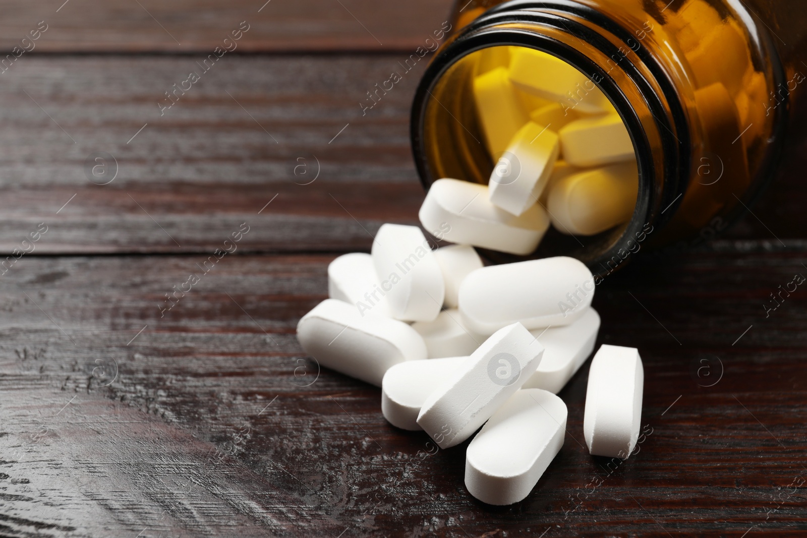 Photo of Bottle and vitamin pills on wooden table, closeup. Space for text