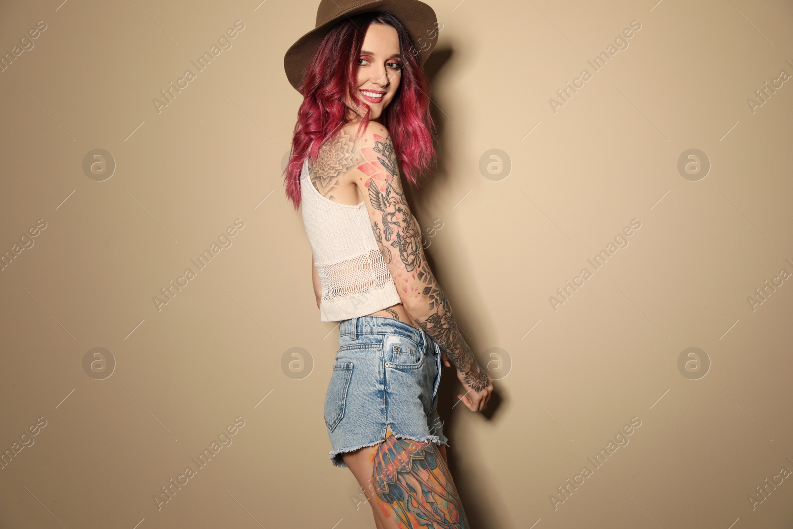 Photo of Beautiful woman with tattoos on body against beige background