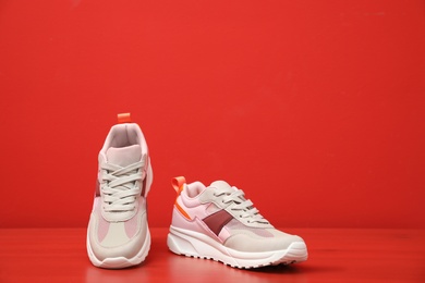 Photo of Stylish women's sneakers on wooden table near red wall