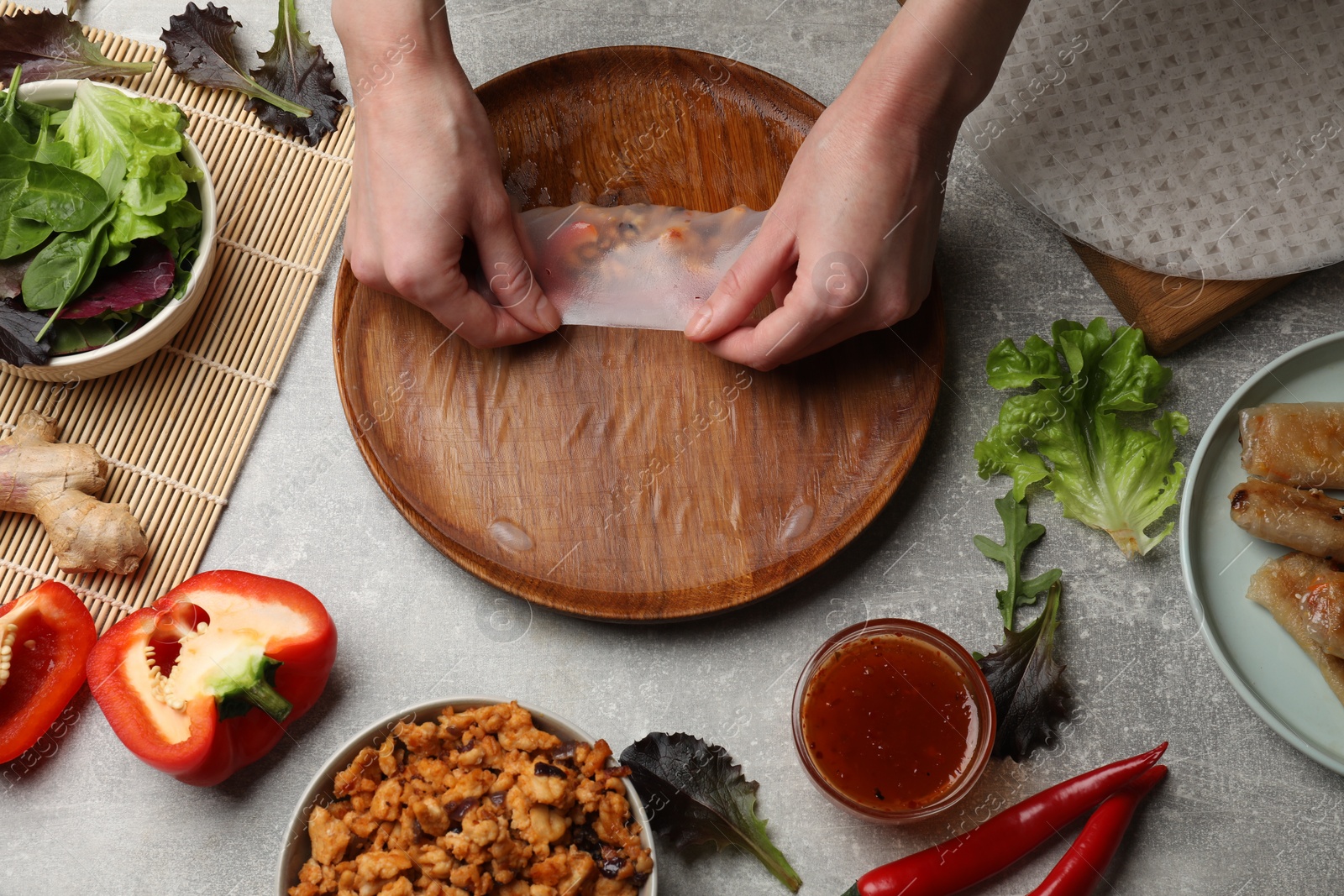 Photo of Woman making tasty spring roll at grey table, top view