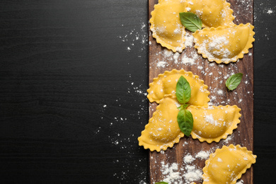 Raw ravioli with basil on black wooden table, flat lay and space for text. Italian pasta